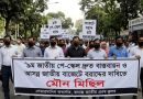 Crowd of Protesters Wearing Masks March Down a Street Holding a Large Bengali Banner