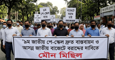 Crowd of Protesters Wearing Masks March Down a Street Holding a Large Bengali Banner