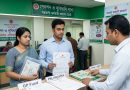 a Man and a Woman Stand at a Government Service Center Counter Holding Documents While a Staff Member Assists Signs on the Desk Include Gp Fund and Other Labeled Form Folders