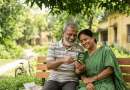Elderly Indian Couple Sits on a Park Bench Smiling While Reading a Small Green Book Together