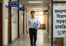 A man in a light shirt and dark pants walks down a government office hallway, carrying a blue folder; Bengali department signs line the corridor.