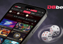 Smartphone showing a betting gaming app UI with colorful game tiles and a DBbet logo in the corner, with rolling dice beside the device